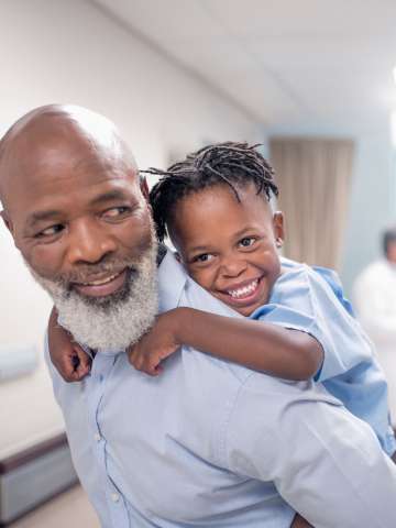 Bearded father giving piggyback to son at children's hospital.