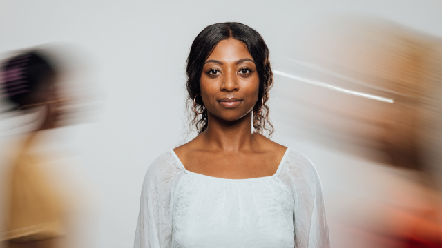 A woman looking at the camera with two people blurred in motion behind her