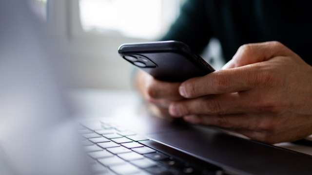 Man holding a smartphone and sitting in front of his computer