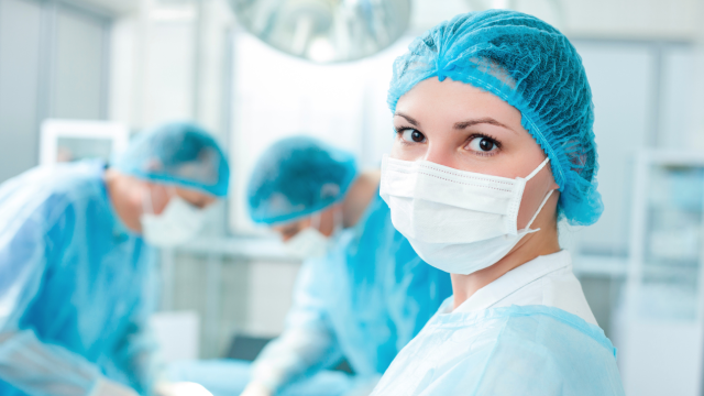 Female doctor in operating room, with two male doctors behind her, actively operating.