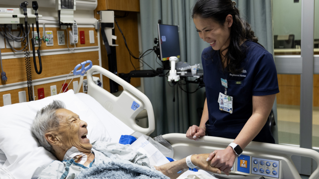 A patient lying in a hospital bed and smiling, while a UCLA Health nurse holds his hand 
