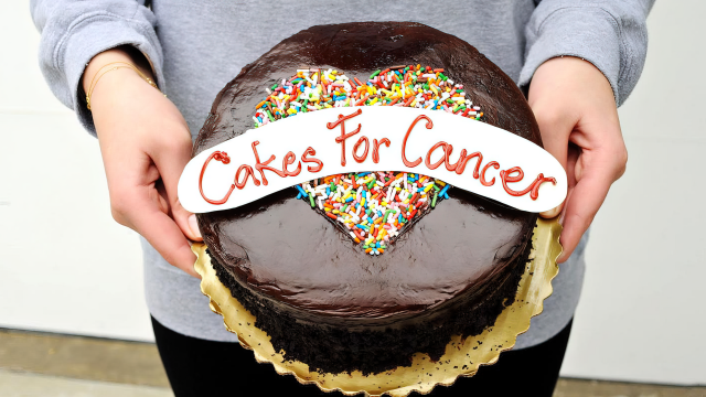 Cakes for Cancer founder Abigail Nathanon holding a chocolate cake, with "Cakes for cancer" written on top