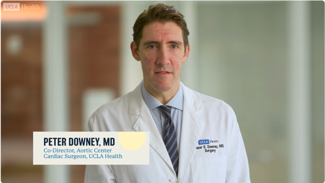 Doctor in white coat and tie with on-screen lower-third name caption