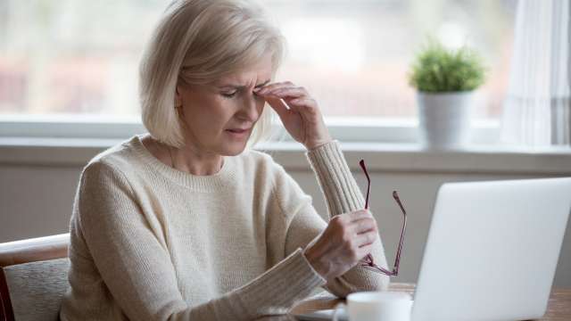 A woman taking off her glasses and rubbing at her eye