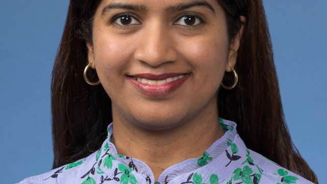 Headshot of a woman with long dark hair, wearing a floral blouse against a blue background.