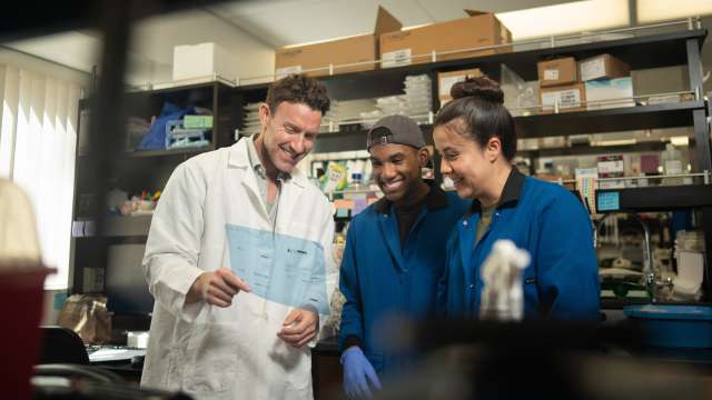 Researcher in lab coat reviewing clipboard with two colleagues in laboratory