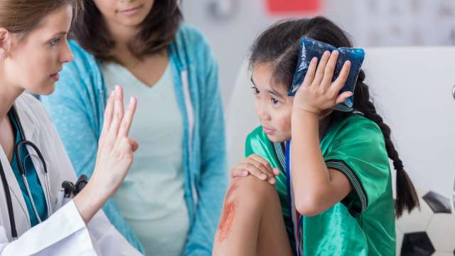 Doctor tests vision of girl holding ice pack to her head as her mother looks on. 