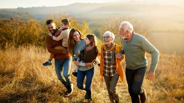 Family walking up hill: multigenerational group climbing a grassy slope at sunset
