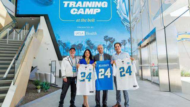 Fred Maas, Johnese Spisso, Dr. John Mazziotta, and Dr. Nicholas Bernthal at Chargers training camp holding No. 24 T‑shirts