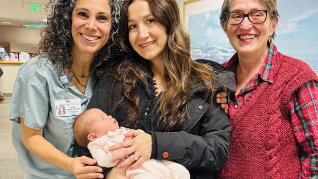 A new mom holds her baby, with her doctor and her own mother by her side.