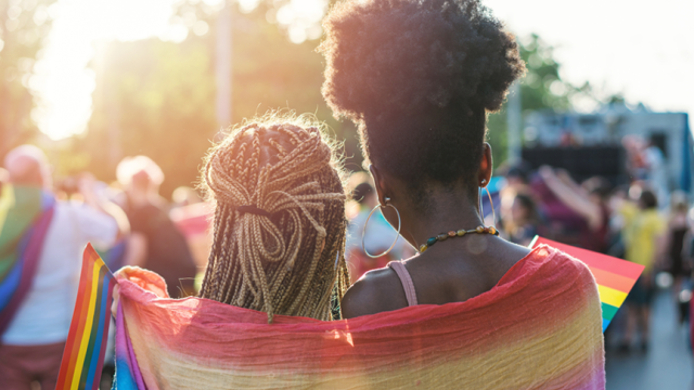 Two people standing with their backs facing us, wearing a flag draped over their shoulders