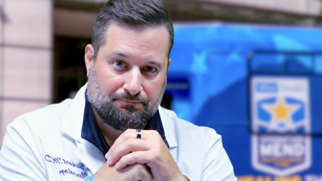 Dr. Bickart in a coat with hands clasped, in front of an Operation Mend branded bus