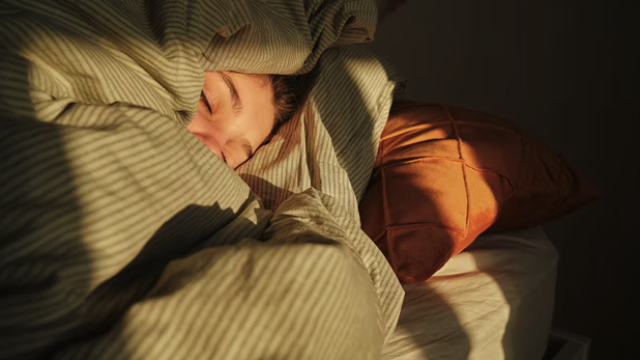 A person in bed covering themselves in a gree bed sheet