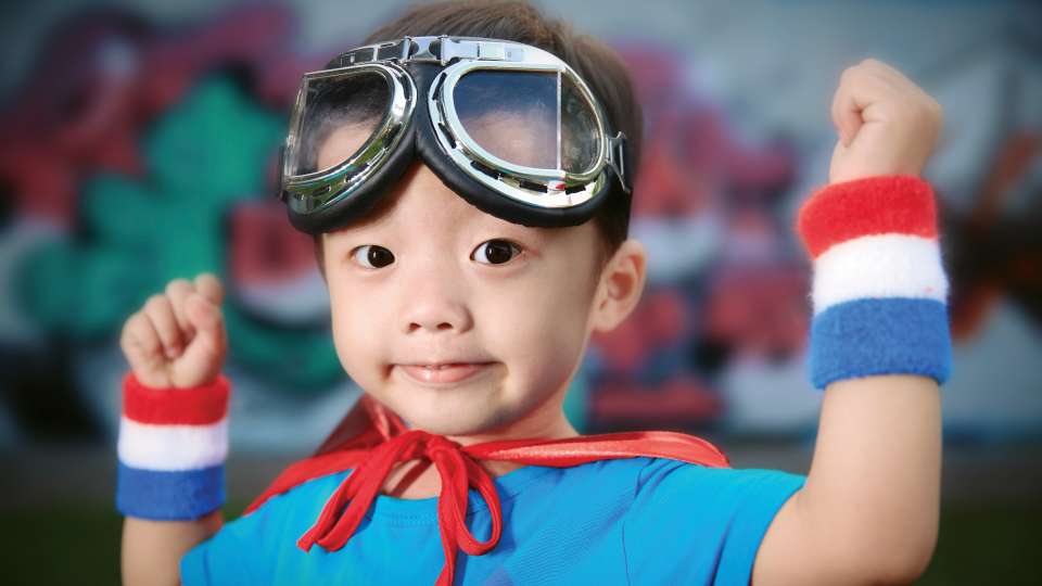 Child standing with arms up wearing goggles on their head