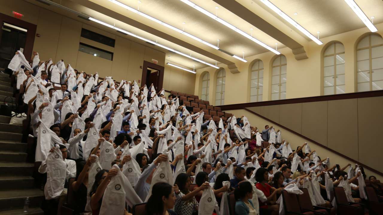 A lecture hall of new medical students holding white coats
