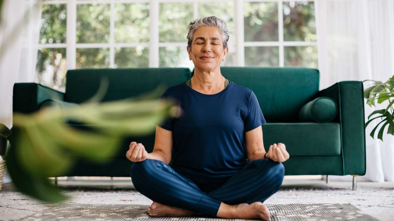 An older woman sits on the floor while meditating.