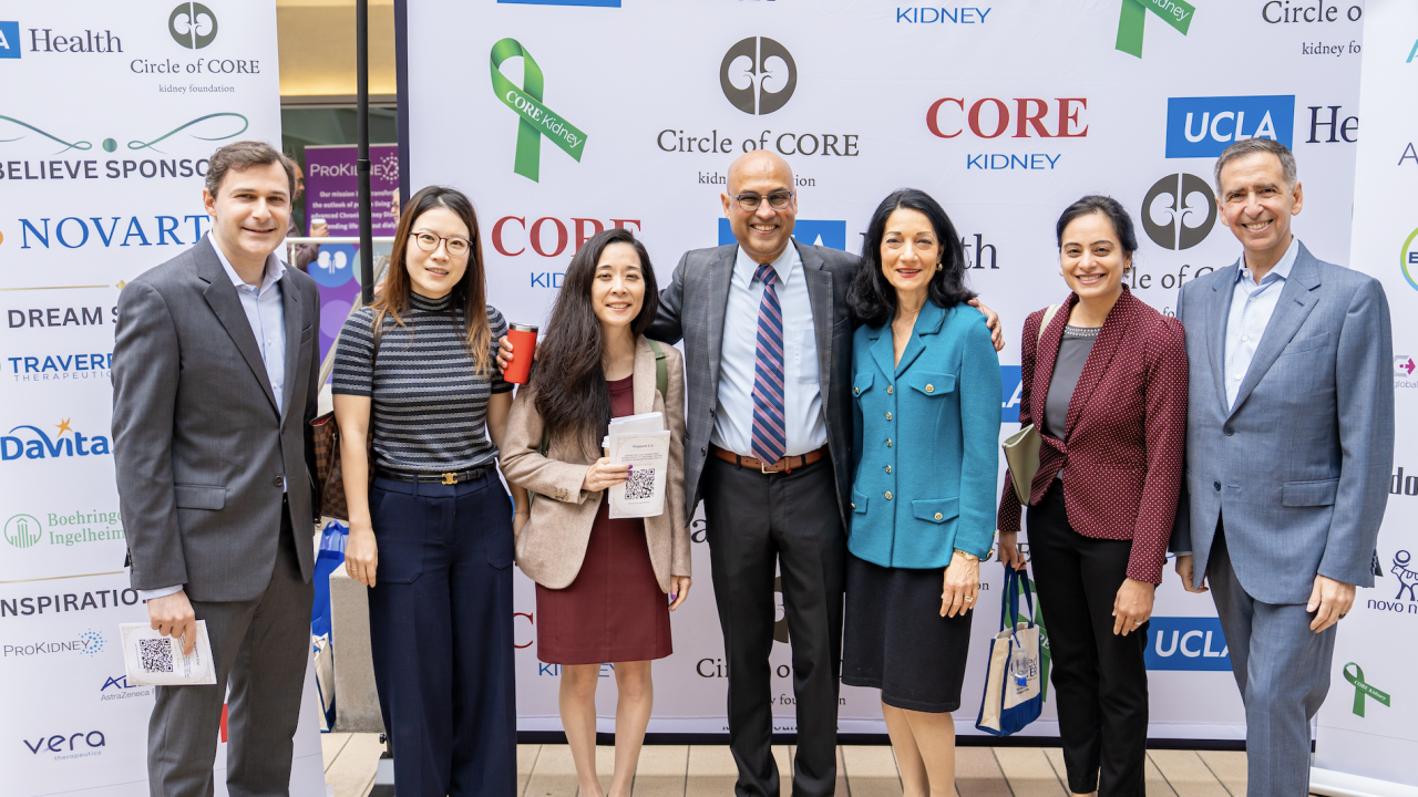 Seven people pose together at an event, smiling in front of sponsor banners.