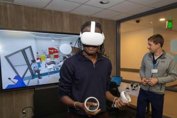 Anesthesiology administrative specialist Jibril Osumanu, left, wears a VR headset for an immersive 3D medical simulation scenario alongside Daniel Weisman, simulation center learning experience designer and station facilitator. 
