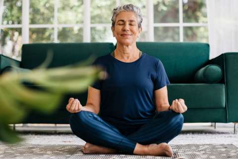 Senior woman meditating in lotus position at home.
