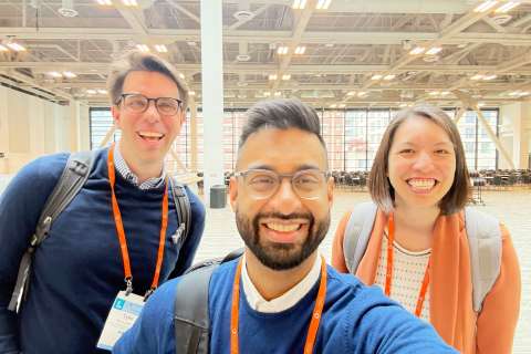 Three people wearing event lanyards taking a selfie in an indoor event space