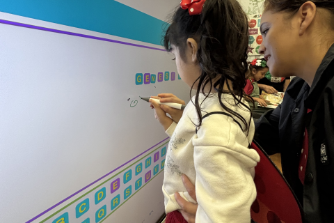 A woman shows a young child how to draw with a marker on a board.