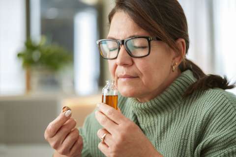 Woman with glasses smelling perfume from a small glass bottle