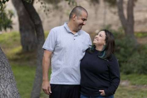 A smiling Lazaro Barajas looks at his wife, who smiles back at him. They are standing outdoors.