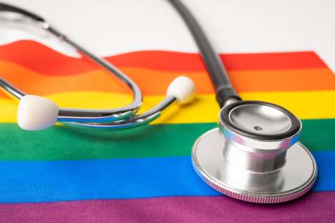 A close-up shot of a silver stethoscope lying on top of a vibrant Rainbow Pride Flag, symbolizing healthcare advocacy for the LGBTQ+ community.