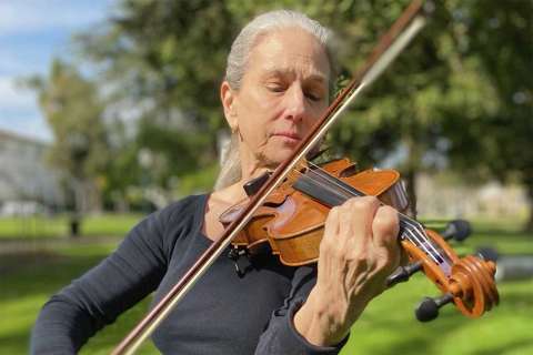 Constance Meyer, a veteran session musician, playing a violin on the grass.