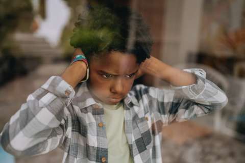 Child holding hands to ears, looking down with a serious expression.