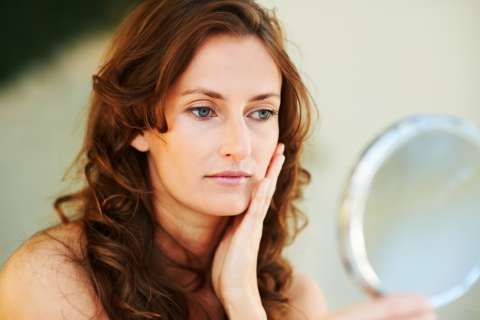 Woman examining her face in a handheld mirror, touching her cheek