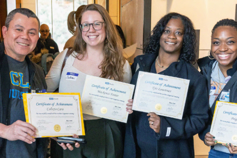 Four individuals holding certificates at a gathering.
