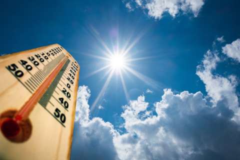 A close-up of a thermometer is shown under a sunny sky.