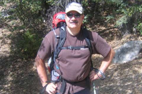 Mark Felling in hiking gear with red helmet and backpack on a sunlit rocky trail