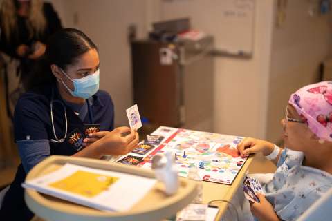 A doctor and pediatric patient play a board game in a hospital room.