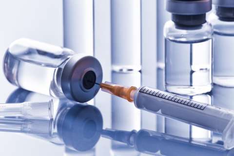 Syringe with needle beside medical vials on reflective surface.