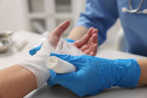 A health care provider wraps an injured hand in gauze.