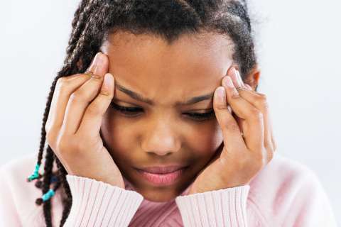 A young girl with a headache touches the sides of her forehead.
