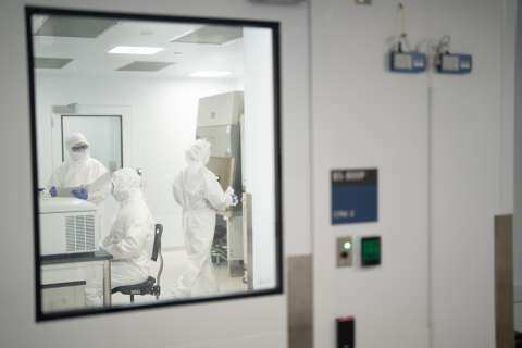 People in white protective suits inside a lab seen through an observation window