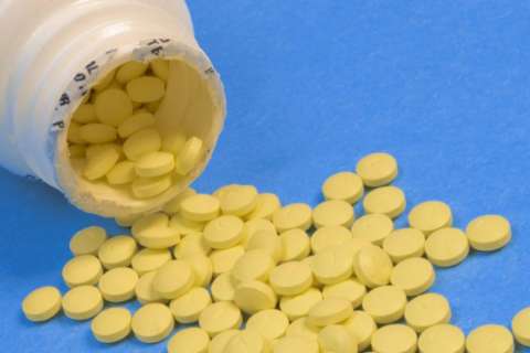 White bottle tipped over with numerous small yellow tablets scattered on a blue surface.