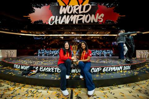 Two women hold a trophy in front of a World Champions sign.