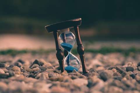 An hourglass stands on a patch of gravel.