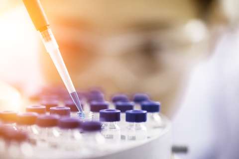 Pipette dispensing liquid into blue-capped microtube rack in a laboratory