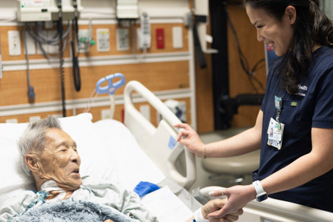 Nurse assisting an elderly patient in a hospital bed.