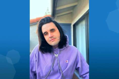 A person wearing a purple hoodie stands outdoors near a building.