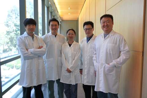 Scientist Lili Yang and four of her lab members in lab coats standing in a windowed corridor