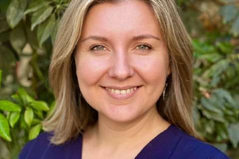 Portrait of Olena Svetlov wearing blue scrubs and standing in front of foliage.