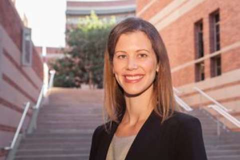 Elisa Long standing on steps, dressed in a black blazer with a blurred face.