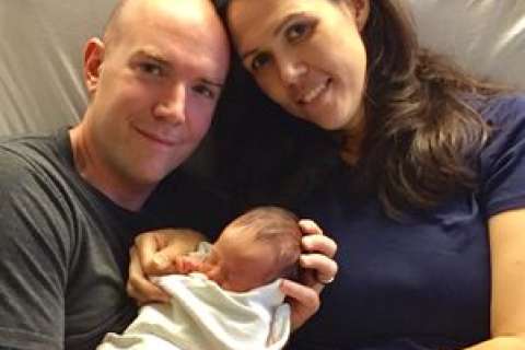 A couple holds their newborn baby, both smiling gently in a hospital setting.