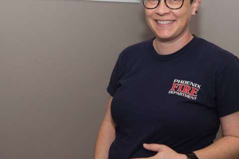Person wearing a dark T-shirt with “Phoenix Fire Department” logo, standing against a plain wall with hands visible.